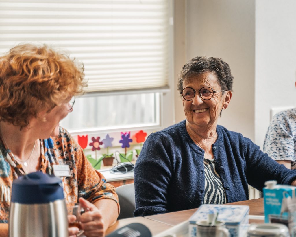 Bewoner en medewerker lachend aan tafel